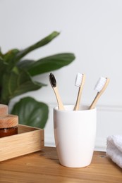 Photo of Bamboo toothbrushes in holder, towel, cosmetic products and leaves on wooden table