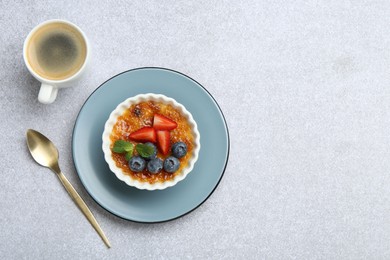 Delicious creme brulee with berries and mint in bowl served on grey textured table, flat lay. Space for text