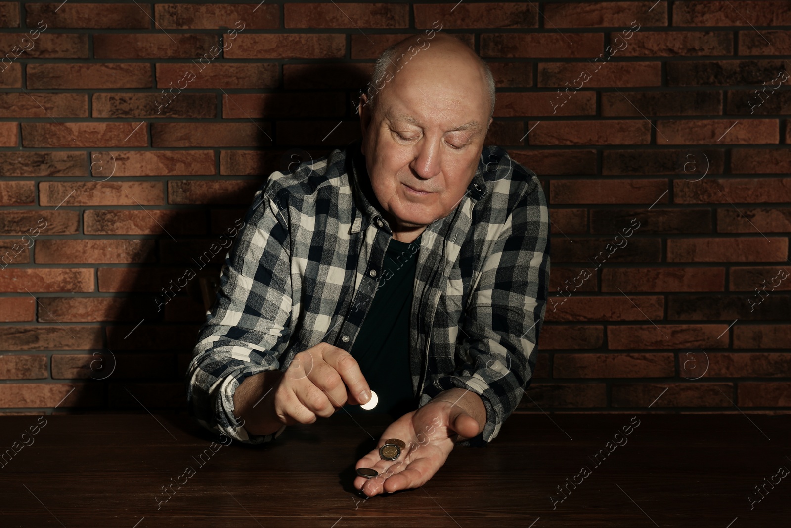 Photo of Poor senior man counting coins at table near brick wall