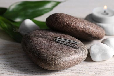Photo of Stones with acupuncture needles on white wooden table, closeup
