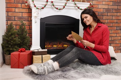 Photo of Young woman with greeting card sitting near fireplace indoors