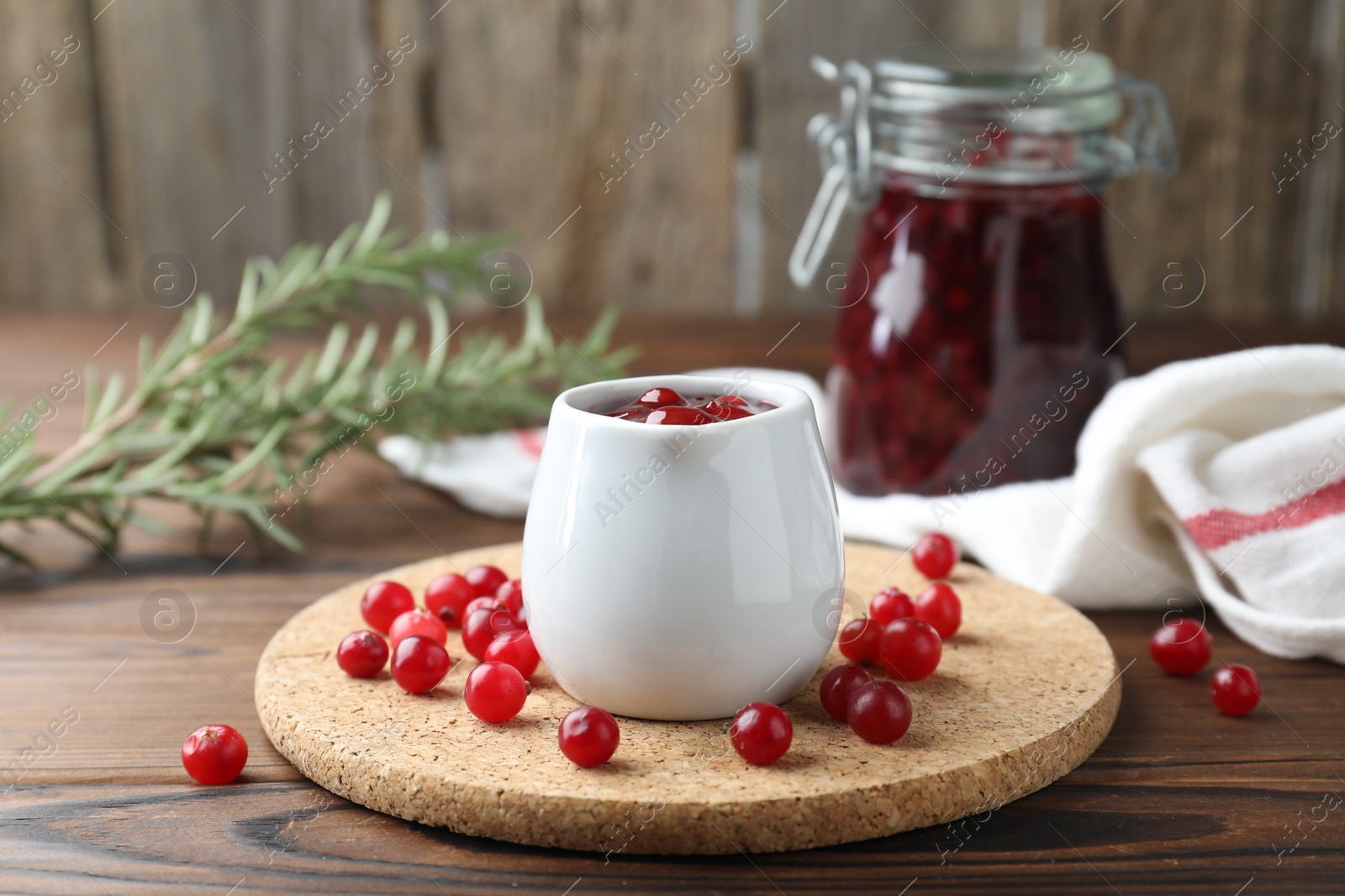 Photo of Cranberry sauce in pitcher and fresh berries on wooden table