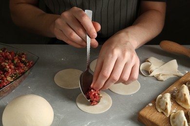 Photo of Woman putting gyoza filling in center of dough wrapper at grey table, closeup