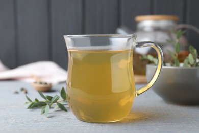 Glass cup of aromatic eucalyptus tea on grey wooden table, closeup