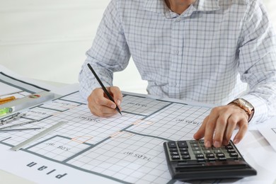 Architect working with construction drawings and calculator indoors, closeup
