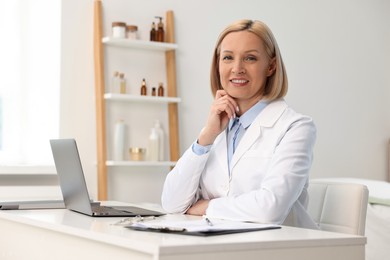 Portrait of happy dermatologist at white table in clinic