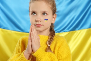Little girl with clasped painted hands near Ukrainian flag
