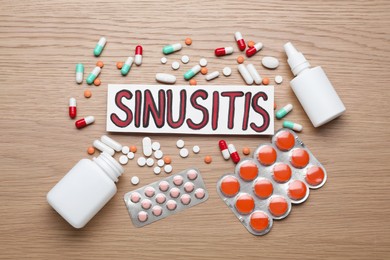 Photo of Card with word Sinusitis, drops, nasal spray and pills on wooden table, flat lay