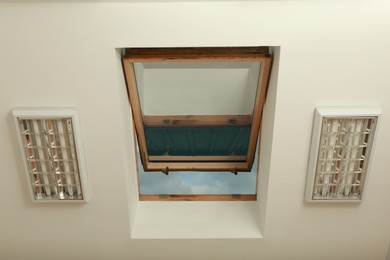 Photo of Open skylight roof window on slanted ceiling in attic room, bottom view