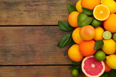 Different citrus fruits with green leaves on wooden table, flat lay. Space for text