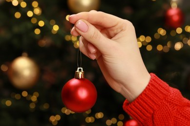 Photo of Woman holding Christmas ball against blurred lights, closeup