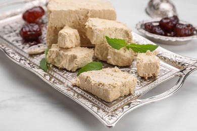 Photo of Pieces of tasty halva, dates and mint leaves on white marble table, closeup