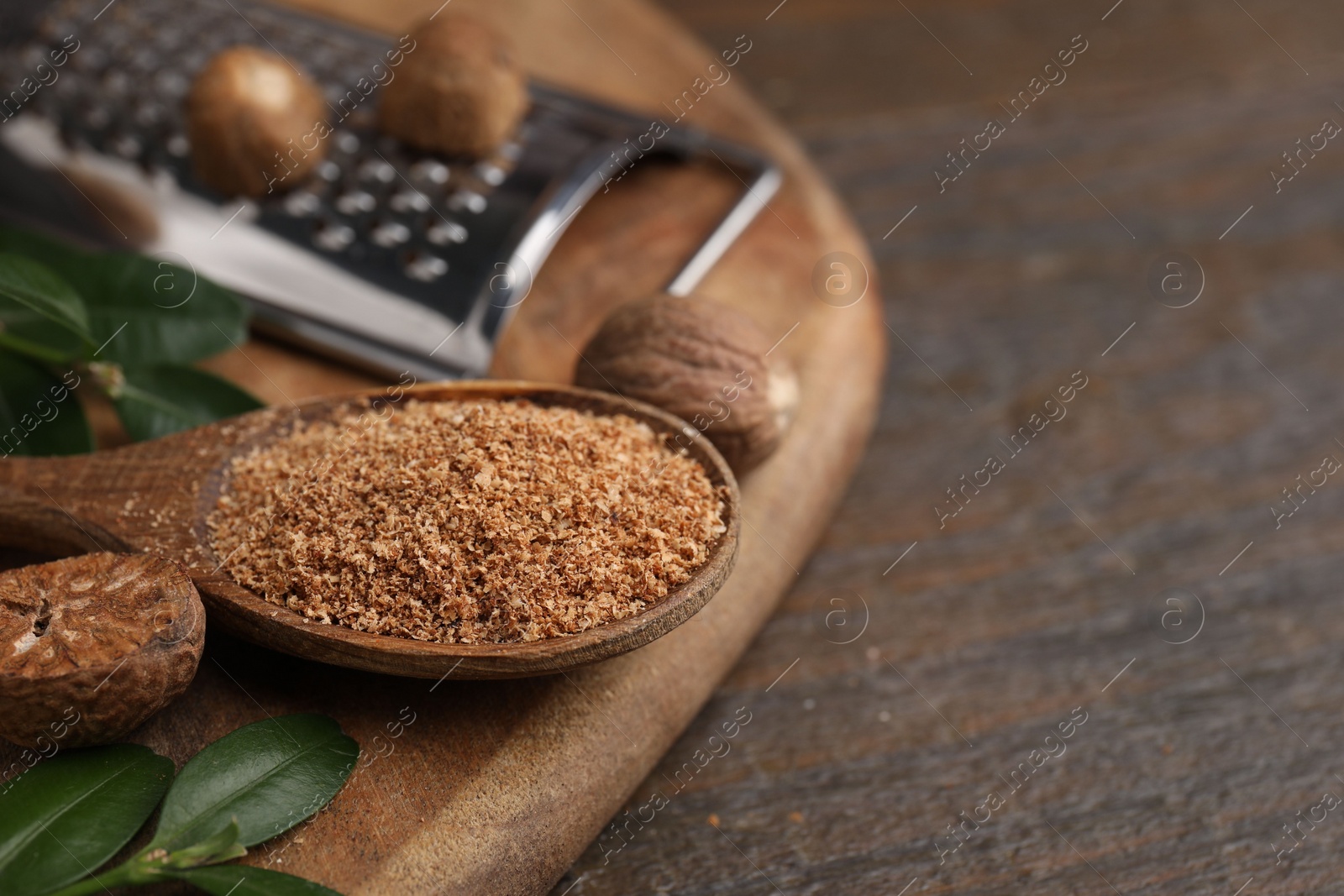 Photo of Spoon with grated nutmeg and green leaves on wooden table, closeup. Space for text