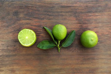 Photo of Whole and cut fresh ripe limes with green leaf on wooden table, flat lay
