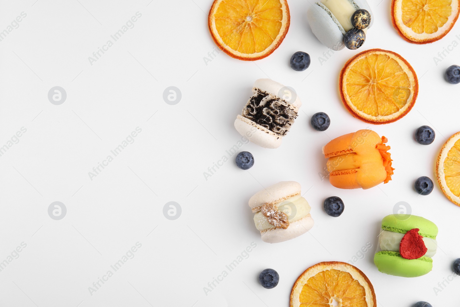 Photo of Delicious macarons, dry orange slices and blueberries on white table, flat lay. Space for text