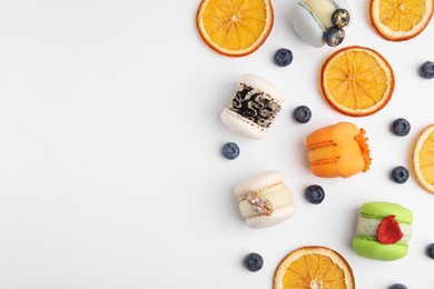 Delicious macarons, dry orange slices and blueberries on white table, flat lay. Space for text