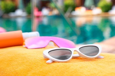 Photo of Sunglasses and sunscreen on beach towel near outdoor swimming pool at luxury resort, closeup. Space for text