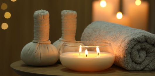 Photo of Spa composition. Herbal bags, towel and burning candle on wooden table, closeup