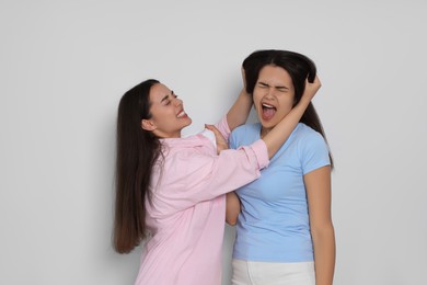 Aggressive young women fighting on light grey background