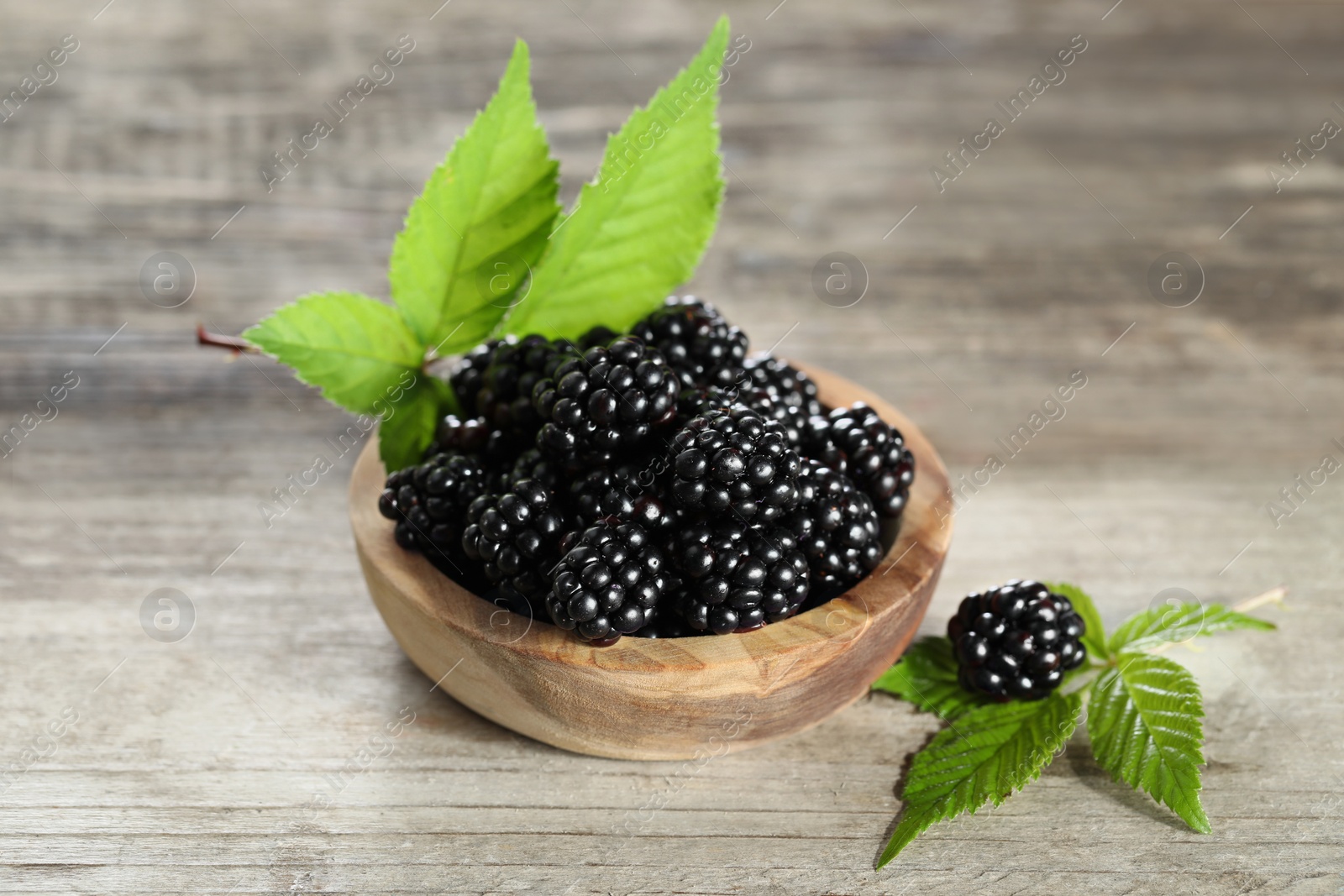 Photo of Ripe blackberries and green leaves on wooden table, closeup