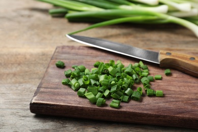 Photo of Wooden board with cut green onions on table