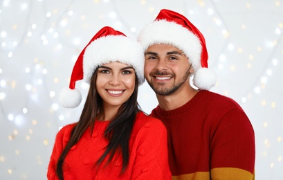 Photo of Lovely young couple in Santa hats against blurred festive lights. Christmas celebration