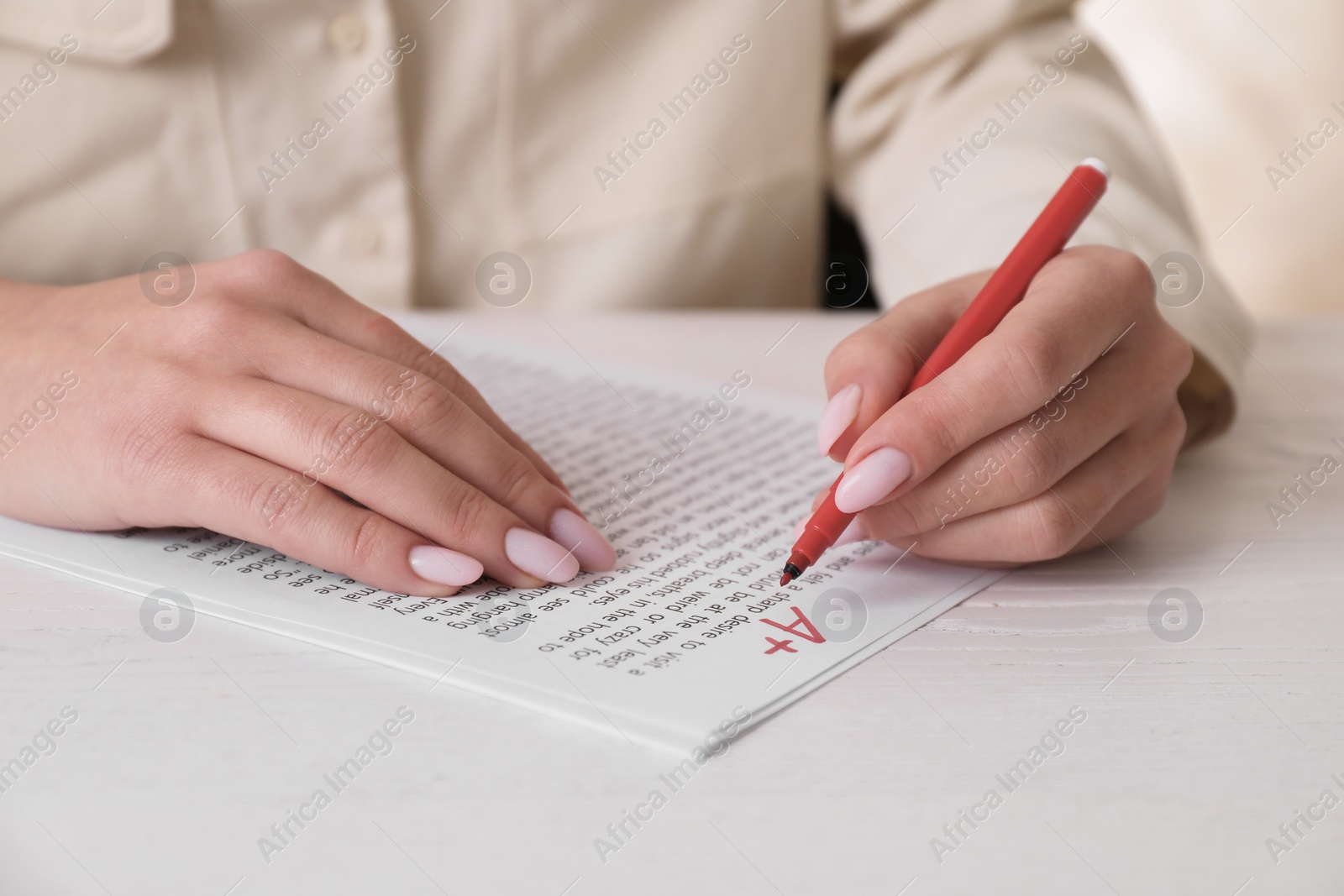 Photo of School grade. Teacher writing letter A with plus symbol on sheet of paper at white table, closeup