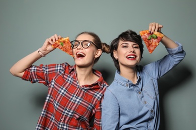 Attractive young women with slices of delicious pizza on color background