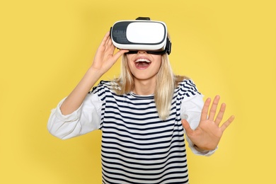 Emotional woman playing video games with virtual reality headset on color background