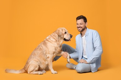 Photo of Cute Labrador Retriever giving paw to happy man on yellow background
