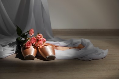Photo of Ballet shoes. Elegant pointes and bouquet of roses on wooden floor indoors, space for text
