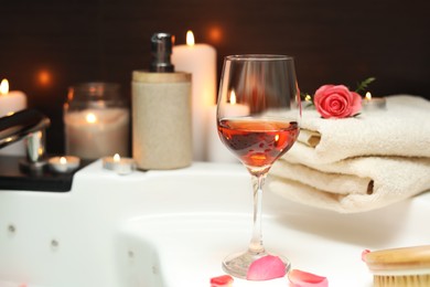 Photo of Wine in glass, towels and rose on edge of bath indoors. Romantic atmosphere