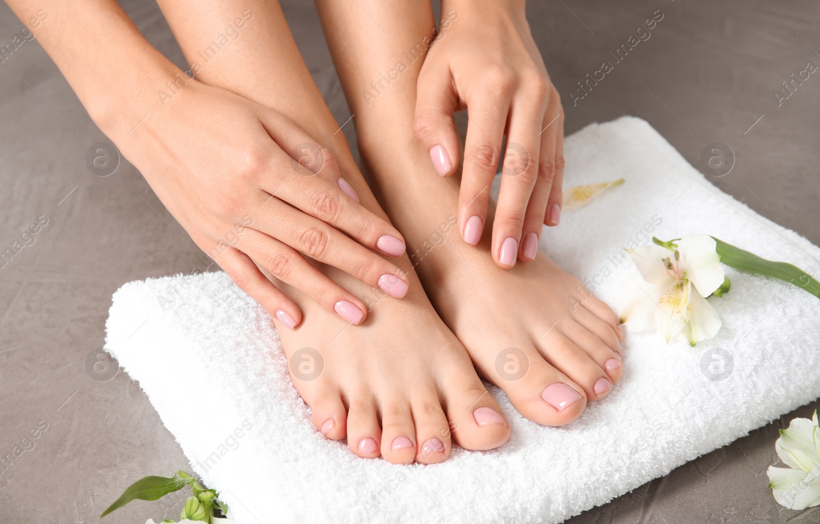 Photo of Woman touching her smooth feet, towel and flowers on grey background, closeup. Spa treatment