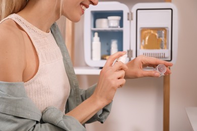 Photo of Woman taking cosmetic product from mini fridge indoors, closeup