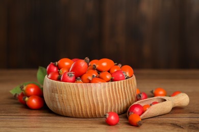 Ripe rose hip berries with green leaves on wooden table