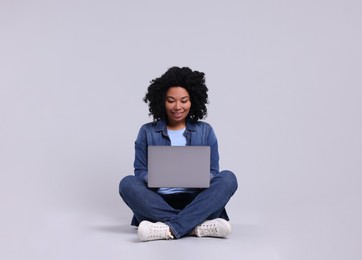 Happy young woman with laptop on light grey background