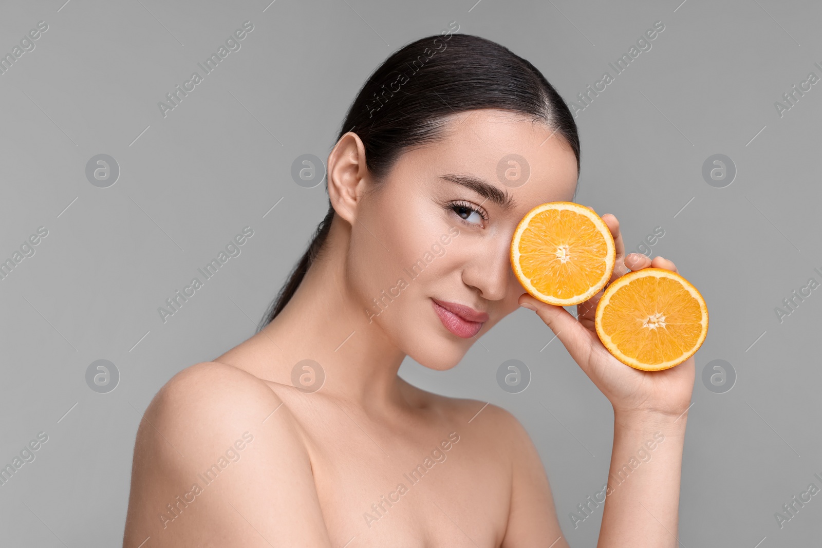 Photo of Beautiful young woman with pieces of orange on grey background