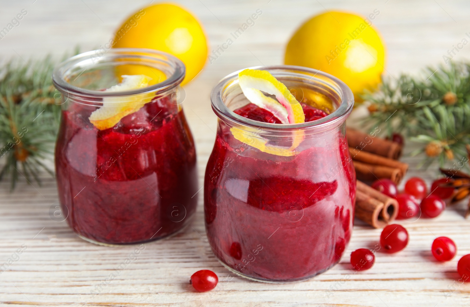 Photo of Tasty cranberry sauce with citrus zest in glass jars on table