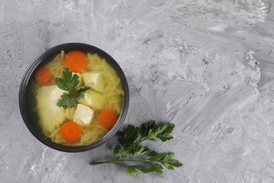 Photo of Tasty chicken soup with noodles, carrot and parsley in bowl on grey textured table, top view. Space for text
