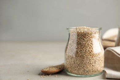 Photo of Jar and wooden spoon with white quinoa on light grey table. Space for text