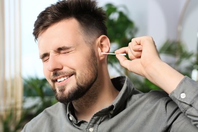 Young man cleaning ear with cotton swab at home