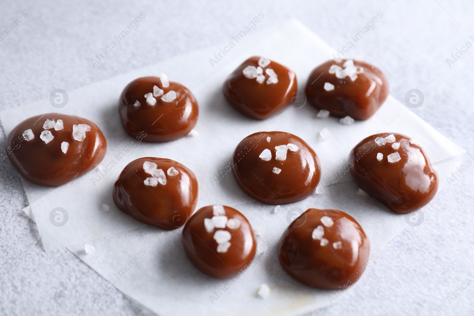 Photo of Tasty caramel candies and salt on light grey table