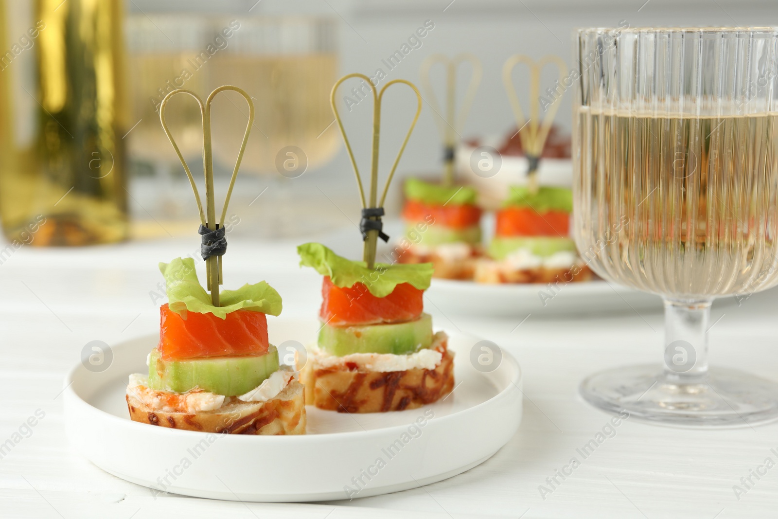 Photo of Tasty canapes with salmon, cucumber, bread and cream cheese served on white wooden table, closeup