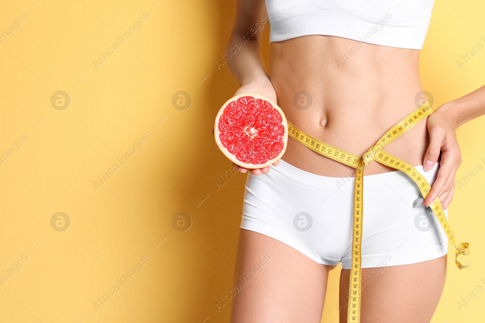 Photo of Young slim woman in underwear with measuring tape and grapefruit on color background. Weight loss diet results