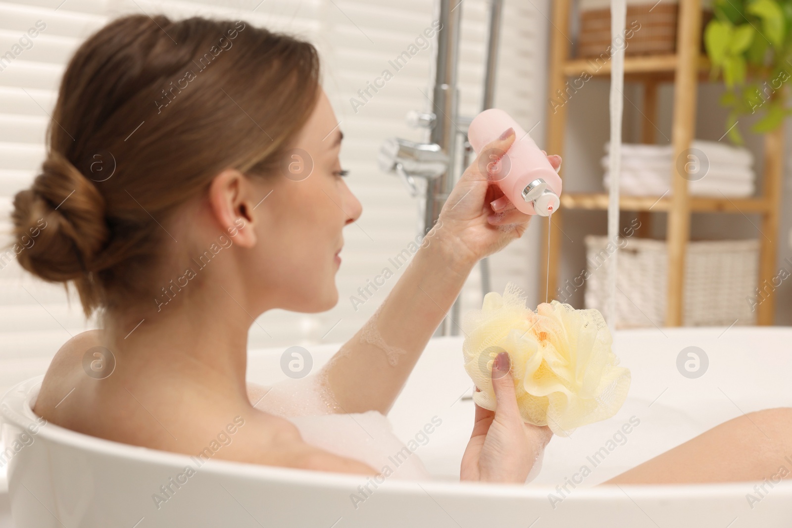 Photo of Woman pouring shower gel onto mesh pouf in bath indoors