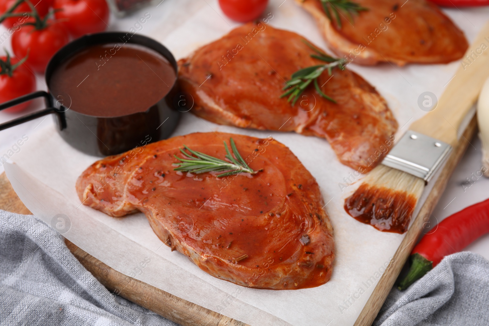 Photo of Raw marinated meat, rosemary and basting brush on table, closeup