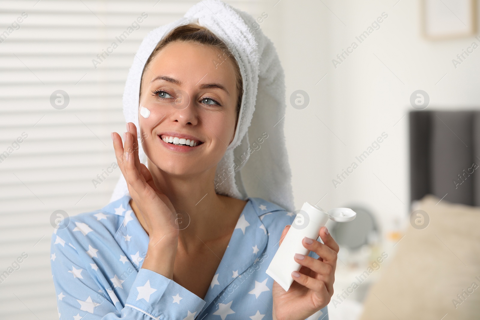 Photo of Young woman applying cream onto her face at home, space for text. Spa treatments