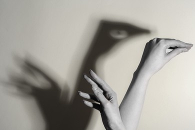 Shadow puppet. Woman making hand gesture like swan on light background, closeup. Black and white effect