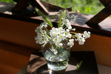Bouquet of beautiful wildflowers in glass vase on book, closeup