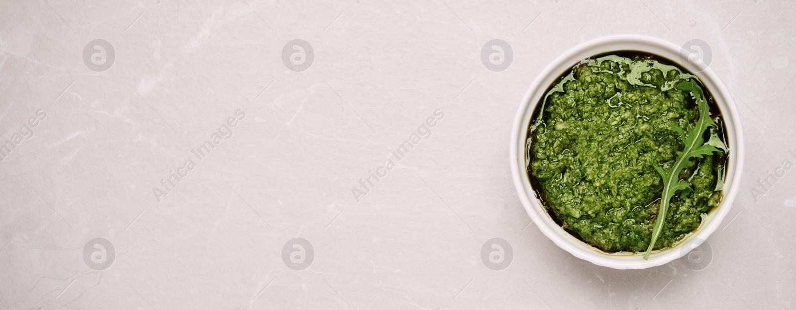Image of Bowl of tasty arugula pesto and space for text on light table, top view. Banner design